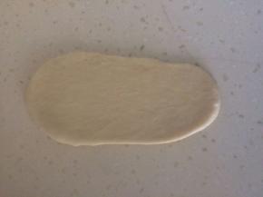 取出一份面团，用排气擀面杖擀成椭圆形，用刮刀翻面，横向放置，用手指将靠下一边搓薄。