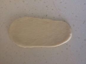 取出一份面团，用排气擀面杖擀成椭圆形，用刮刀翻面，横向放置，用手指将靠下一边搓薄。