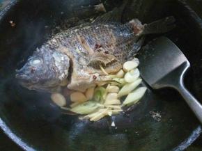 留少许余油，把鱼推至锅边。放入烧鱼料炒香，在鱼身上淋入料酒。