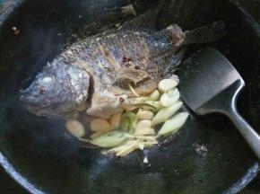 留少许余油，把鱼推至锅边。放入烧鱼料炒香，在鱼身上淋入料酒。
