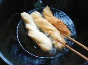 面胚定型后用中火，用筷子压住翻滚油条，使各面炸透。