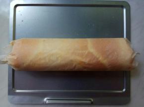 蛋糕连着油纸，拉到烤网上，翻面，撤出油纸。晾至温热，翻面正面朝上，再换油纸，从一头开始卷紧，向前卷成卷。蛋糕卷放入冰箱冷藏一小时定型。