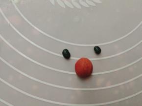 取10克的红色面团做出鼻子，准备两粒黑豆当做眼睛