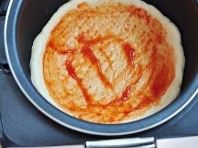 面团擀成圆饼状，放入内胆中铺均匀，用叉子叉出气孔，抹一层番茄酱。