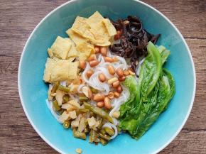 装米粉的碗中倒入各种配菜包，酸笋、酸豆角、萝卜干、腐竹片、花生米，将煮好的生菜叶捞出放入碗里