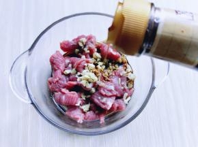 切好的牛肉片放入容器中，加入切好的姜末和蒜末，再加入生抽。