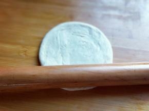 将小面团立再面板上，用手心压扁，然后再用擀面杖擀开，约12cm左右圆形。