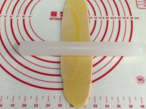 取一份静置好的油酥皮，用手压扁，用擀面杖再一次从中间往两头擀开。