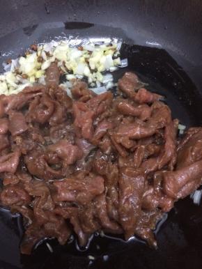 把炒香的葱、姜、蒜用铲子铲到一边，在把腌好的牛肉放入锅中，炒到肉变色

