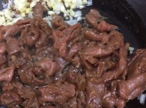 把炒香的葱、姜、蒜用铲子铲到一边，在把腌好的牛肉放入锅中，炒到肉变色

