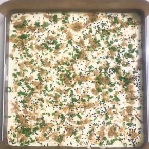 取三分之蛋白糊加入蛋黄糊中，用手动打蛋器快速Z字型搅拌均匀，全部加入蛋白糊继续用手动打蛋器快速Z字型搅拌均匀，最后用刮刀从底下彻底翻伴均匀，倒入铺上油布的烤盘里，借用刮刀抹平，拿起模具震几下，震去气泡，表面洒上肉松香葱芝麻