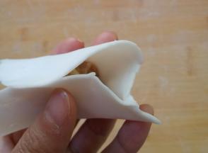 右手食指顶住饺子皮，向前捏褶。