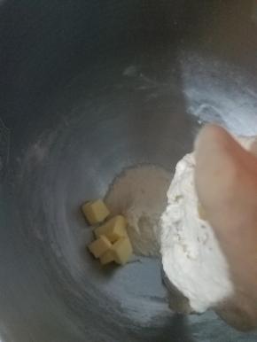 加入软化好的黄油，然后把面团撕小块先低速搅拌8分钟，然后把桶壁的面块刮下来再中速转高速搅拌5分钟