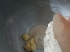 加入软化好的黄油，然后把面团撕小块先低速搅拌8分钟，然后把桶壁的面块刮下来再中速转高速搅拌5分钟