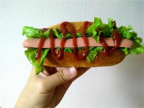 将凉了的热狗胚竖向切开，不要切断，夹上一点生菜叶和半根香肠，挤上番茄酱，一个热狗就做好了。