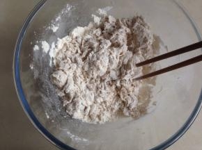 一边倒入豆浆酵母水，一边用筷子搅拌面粉，成絮状