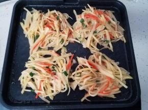 把搅拌好的土豆丝取出四小份，放在煎烤盘上，然后在上面撒上少许芝麻。