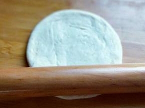 将小面团的两头捏紧。将小面团立再面板上，用手心压扁，然后再用擀面杖擀开，约12cm左右圆形。