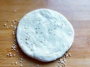 再面板上撒上少许熟白芝麻，把做的饼胚放在芝麻上压一下，使面团沾满芝麻。