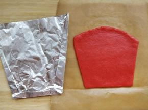 将红色面团在两层油纸间擀成3mm厚片之后，根据锡纸裁出稍大一点的形状