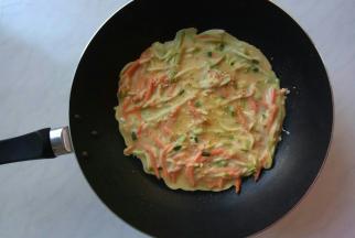 小火，煎锅里抹一点油，倒入一勺面糊快速转动锅子，面糊可以自由流动到锅里四周。用筷子轻轻地把面皮表面蔬菜扒拉均匀，均匀地撒上芝麻，注意不要弄破面皮。