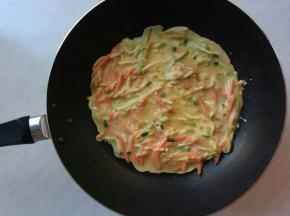 小火，煎锅里抹一点油，倒入一勺面糊快速转动锅子，面糊可以自由流动到锅里四周。用筷子轻轻地把面皮表面蔬菜扒拉均匀，均匀地撒上芝麻，注意不要弄破面皮。