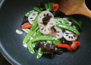 依次下入荷兰豆、藕片、红椒、木耳，翻炒。加味极鲜、盐、糖调味。