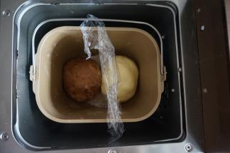 将面包桶里的搅拌刀取出，将两份面团滚圆后放入，中间放入保鲜膜隔开，选择面包机的发酵程序40分钟