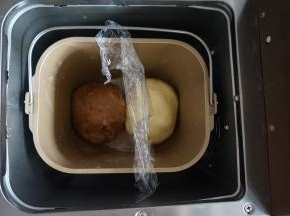 将面包桶里的搅拌刀取出，将两份面团滚圆后放入，中间放入保鲜膜隔开，选择面包机的发酵程序40分钟