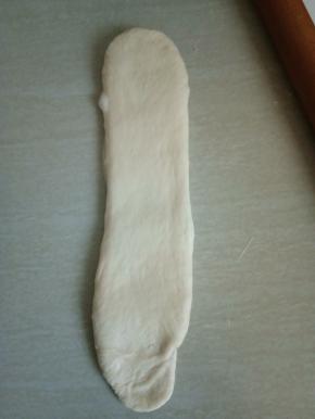 将第二次松弛好的面团再次擀成长舌状。翻面，由上往下卷起。