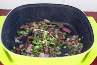 腌制好的牛肉倒入锅中翻炒，加入洋葱、辣椒、香葱等炒熟；