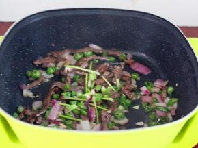 腌制好的牛肉倒入锅中翻炒，加入洋葱、辣椒、香葱等炒熟；