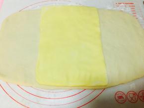 按扁后的面团，擀平，大小左右可以包裹住黄油片即可。将之前整理好的黄油片，放在中间位置。这里需要格外注意的是，黄油的软硬程度不要太硬。用手按压黄油片，使其与面片更好的粘合。黄油片上下与面片对齐。是的！对齐，不用包裹。