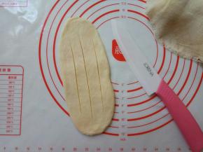 按扁，擀成牛舌状，用锋利的刀在面皮表面划三刀。