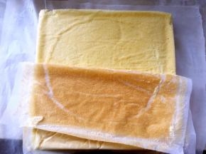 凉至不烫手时，另外铺一张油纸，将蛋糕卷倒扣在油纸上，揭下底部的油纸