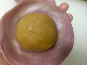 如图，取一个静置好的面卷，立起来压扁，然后擀成圆形，包入准备好的内馅。重复此步骤将所有蛋黄酥包好。排入烤盘中。