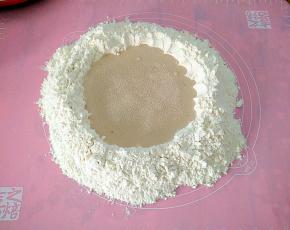 把面粉倒在案板上，中间挖出来一个坑，再把泡打粉撒在面粉的四周，中间加入温水白糖酵母，用手拌匀。