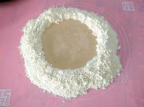 把面粉倒在案板上，中间挖出来一个坑，再把泡打粉撒在面粉的四周，中间加入温水白糖酵母，用手拌匀。