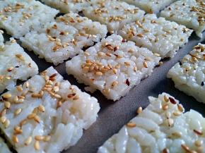 冷冻好的米饭薄片洒芝麻用擀面杖轻压一下，切成等大的薄片，放入不粘烤盘