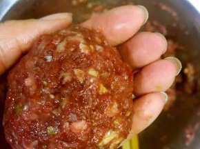5. 电饭煲中放入500克高汤，再加入适量的水，烧至沸腾，取一点肉馅，两手倒换轻摔，直至滚圆，放入锅中，先将按键调至保温