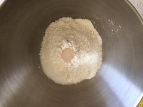 盆内倒入高筋面粉，盐和糖对角线放置，中间挖一小孔倒入活性干酵母