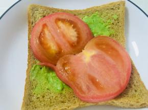 取一片吐司，用勺背抹上适量牛油果泥，然后码几片番茄片