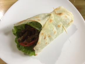 放入炒好的牛肉条，再将饼周围的边缘折起卷起，用牙签固定住即可食用
