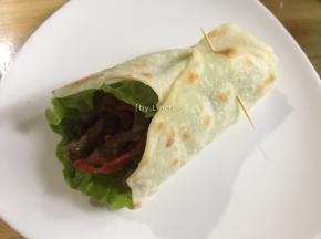 放入炒好的牛肉条，再将饼周围的边缘折起卷起，用牙签固定住即可食用
