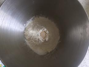 牛奶面团的制作：高筋面粉倒入厨师机面桶，中间挖一小控倒入活性干酵母，盐和糖对角线放置