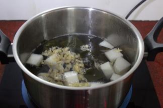 洗净锅，倒入适量的清水，煮沸，放入白萝卜、海带结、花蛤肉、生姜；