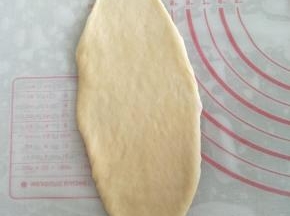 取一个圆面团，用排气擀面棍将面团擀成23CM长的椭圆形。右手用刮板将面团铲起，左手将面团翻面