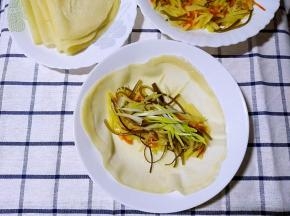 土豆丝炒好之后，拿一张薄饼上放上土豆丝。再放一点儿葱花卷起。
