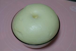 将原料中的高筋面粉300g、奶粉25g、清水140g、鸡蛋液45g、糖40g、盐2g、酵母4g放在一个小盆里，用筷子搅拌均匀后转到到揉面垫上，用手揉至光滑，加入玉米油20g，继续揉至出膜。揉好的面团放在一个容器里，盖上保鲜膜，放置在一个温暖的地方发酵至两倍大。我一般都是放在暖气片上；