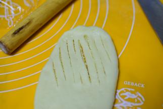 在将包好椰蓉的面团擀成长条状，在一侧划出一厘米宽的道